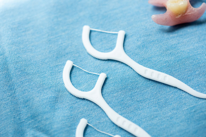 Removable flipper denture and dental floss on blue background. Oral care, dental hygiene, prosthesis concept. Dentistry tool closeup