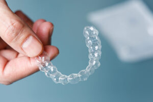 Close-up of a hand holding a clear dental aligner for orthodontic teeth straightening treatment.