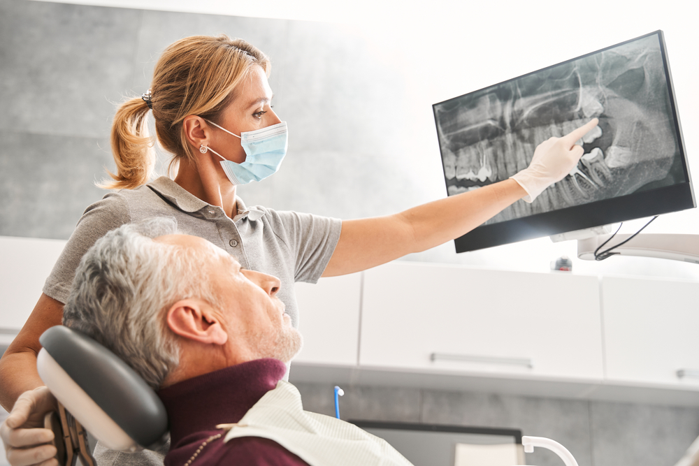 Close up of a single dental implant screw being placed into a patient's lower jaw. Focus on the screw, with the surgeon's hands blurred. No text on image.