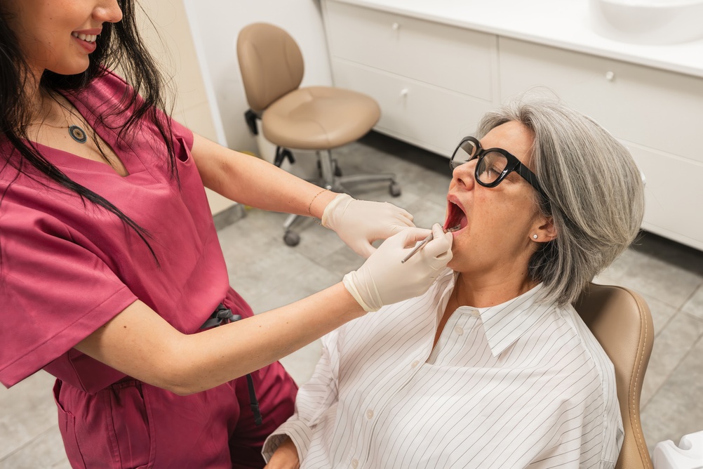 Close up image of a dentist adjusting a dental crown on top of an implant abutment. The dentist is smiling and the patient is comfortable. No text on image.