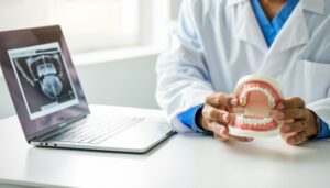 A person in a white lab coat holds a dental model of a mouth with teeth, while sitting at a desk next to an open laptop showing both a dental X-ray image and a content review dashboard.